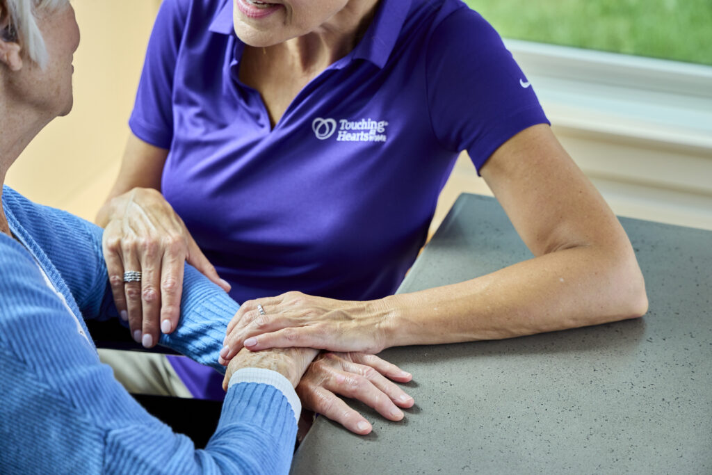Close-up of a Touching Hearts at Home caregiver with her hands on a senior client's, illustrating quality service related to senior care franchise costs.